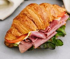 French croissant sandwich with lettuce , cheese , tomatoes and ham photo