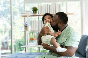 Happy african american man play with little infant toddler child in living room sofa. Parent and little kid relaxing at home. Parents and toddler child girl enjoying spending time at home. Childcare photo