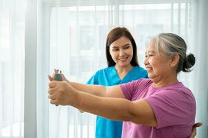 Happy elderly female exercising with rubber expander with Young physiotherapist for recovery arm muscles in a physiotherapy center. Concept of happy retirement with care from a caregiver and health. photo