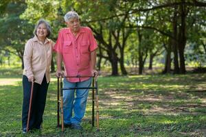 un antiguo mayor asiático hombre usos un caminante y camina en el parque con su esposa. concepto de contento Jubilación con amor y cuidado desde familia y cuidador, ahorros, y mayor salud seguro foto