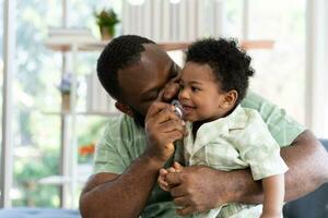 Happy african american man play with little infant toddler child in living room sofa. Parent and little kid relaxing at home. Parents and toddler child girl enjoying spending time at home. Childcare photo