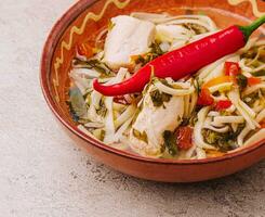 Soup chicken - broth with noodles, herbs, pepper and vegetables on plate photo