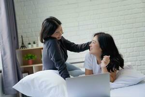 Beautiful asian lesbian LGBTQ couple using computer laptop together smile on bed photo