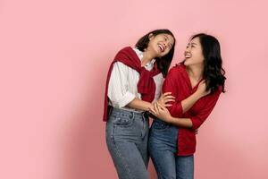 Two happy Asian female friends smiling and having fun teasing on a pink background. photo