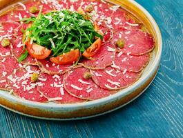 Beef carpaccio with capers, parmesan, arugula and tomatoes photo