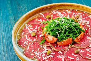 Beef carpaccio with capers, parmesan, arugula and tomatoes photo