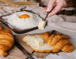 woman hands cut a fresh croissant and spreading butter photo