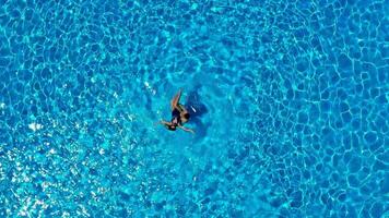 top antenne visie van een vrouw in een blauw zwempak aan het liegen Aan haar terug in de zwembad. Mens cirkelen een vrouw in de water en een vrouw aan het liegen in haar armen. de concept van gelukkig vakantie video