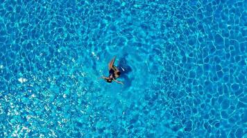 oben Antenne Aussicht von ein Frau im ein Blau Badeanzug Lügen auf ihr zurück im das Schwimmbad. Mann kreisen ein Frau im das Wasser und ein Frau Lügen im ihr Waffen. das Konzept von glücklich Ferien video