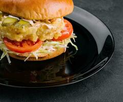 Fried fish fillet burger on black plate photo