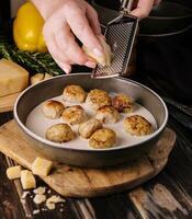 woman grating parmesan on meatballs in cream sauce photo