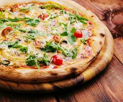 Pizza with arugula, cheese, yoghurt and cherry tomatoes closeup photo