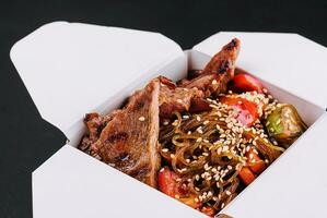 Close-up of noodles in a box with vegetables and beef in teriyaki sauce photo