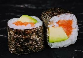 Sushi rollos con salmón y aguacate en un negro Roca foto