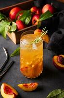 Peach tea with ice and rosemary on a tall glass. Vegan homemade healthy  drink on a dark background with fresh fruits. photo