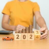2023 flipping to 2024 year block with car model and Coins Money stack for deposit and Automobile Tax. Money Saving, Car Insurance, Financial, vehicle Repair and Maintenance and New Year concept photo
