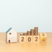 2023 flipping to 2024 year block with house model and Coins stack. real estate, Home loan, tax, investment, mortgage, financial, savings and New Year Resolution concepts photo
