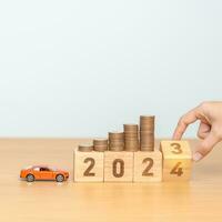 2023 flipping to 2024 year block with car model and Coins Money stack for deposit and Automobile Tax. Money Saving, Car Insurance, Financial, vehicle Repair and Maintenance and New Year concept photo
