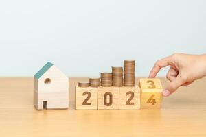 2023 flipping to 2024 year block with house model and Coins stack. real estate, Home loan, tax, investment, mortgage, financial, savings and New Year Resolution concepts photo