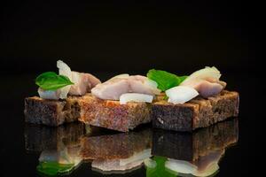 canape of pieces of salted herring with onions on a fresh dark piece of bread. photo