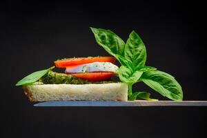 fresh slice of bread with pesto sauce, mozzarella and tomato on a wooden spatula with basil. photo