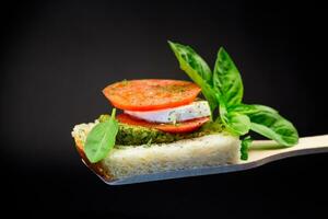 Fresco rebanada de un pan con pesto salsa, queso Mozzarella y tomate en un de madera espátula con albahaca. foto