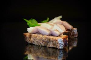 canape of pieces of salted herring with onions on a fresh dark piece of bread. photo