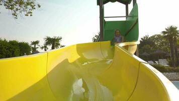 Small cute girl sliding down a water slide at a swimming pool slow motion 4K video