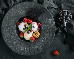 Vanilla ice cream scoops with fresh berries on black plate photo