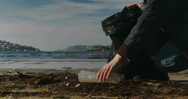 écologiste fille recueille Plastique poubelle sur le côte. Jeune femme recueille Plastique des ordures dans une des ordures sac sur le sablonneux plage de le mer. fille nettoie océan littoral de Plastique bouteille poubelle sur video