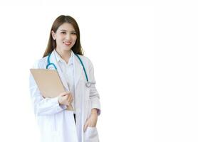 Young professional Asian woman doctor wears medical  white lab coat stand and hold clipboard in her hand at work office in hospital. Coronavirus protection concept. photo