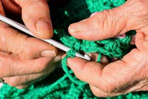 an older woman is knitting a green crocheted bag photo