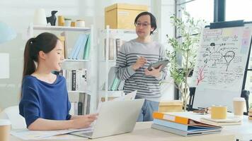 deux Jeune asiatique Commencez entreprise les partenaires discuter et idée de génie dans décontractée petit affaires bureau, commercialisation Planification emplois sur une ordinateur portable, et free-lance travail comme commerce électronique entrepreneur et collaborateur équipe. video