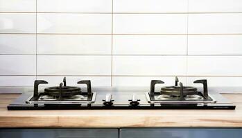 Front view of Contemporary tempered glass gas stove hob with Two burners with auto ignition knob on wooden countertop, cast iron pan supports fan hood and oven built in compact photo