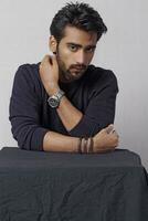 a man with a beard and a watch is sitting at a table photo