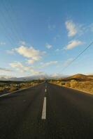 an empty road with power lines and mountains in the background photo