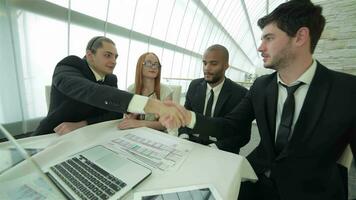 Four smiling successful businessmen sitting at table in office while discussing video