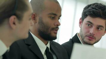 Three smiling successful businessmen sitting at table in office while discussing video