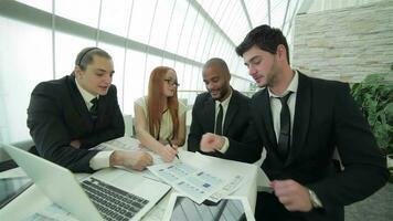 Four smiling successful businessmen sitting at table in office video