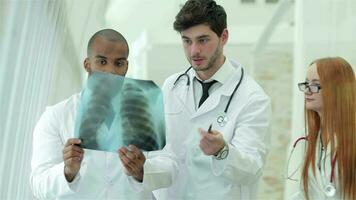 Three confident doctor examining x-ray snapshot of lungs in hospital video