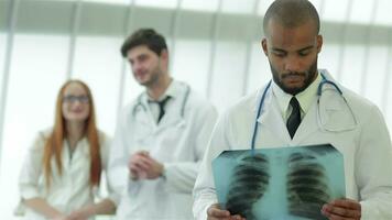 portret van een jong dokter met röntgenstraal in handen Aan achtergrond van twee collega's video