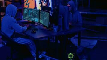 Hackers in dark neon lit underground HQ coding malware designed to exploit network backdoors, using high tech tools to bypass security measures such as logins and password protections video