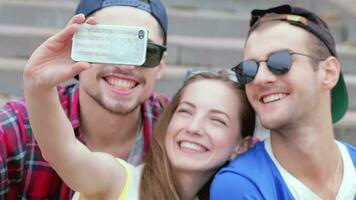 alegre niña sentado en el pasos de su amigos hace selfie video