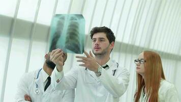 Three confident doctor examining x-ray snapshot of lungs in hospital video