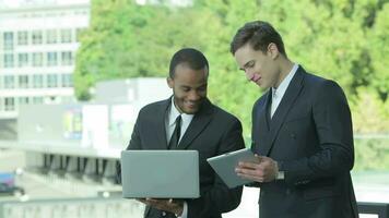 Two confident businessman holding a tablet and a laptop video