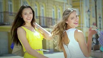 två ung glamorös flickor gå hand i hand med handla påsar video