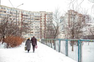 un antiguo hombre y un antiguo mujer caminar a lo largo el patio en invierno en un residencial zona de el ciudad foto