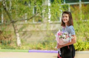 adolescente niña sostiene un ramo de flores de flores y va a escuela. estudiante felicita con De las mujeres día en marzo 8 maestro. Días festivos a escuela. cumpleaños a niño de 11 años. foto