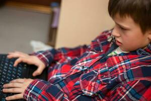 boy in plaid shirt does lessons on laptop. child learns remotely during quarantine of coronavirus. Online learning from home. photo