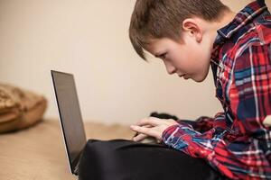 boy in plaid shirt does lessons on laptop. child learns remotely during quarantine of coronavirus. Online learning from home. photo